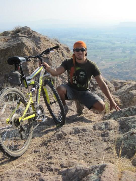 Agachado en una cima rocosa junto a una bicicleta de montaña amarilla